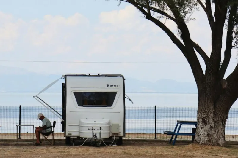 Deniz kenarında ağaç gölgesinde park etmiş karavan
